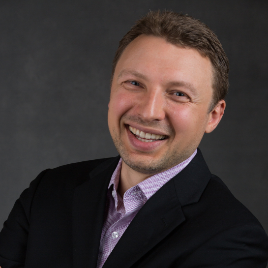 sergey-phd Professional headshot of Sergey, Chief Operating Officer at Stelmakh & Associates, wearing a black blazer and light purple shirt, smiling confidently against a dark gray background.